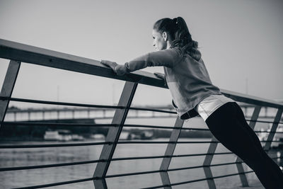 Woman exercising on railing against sky