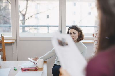 Woman looking at female friend with paper in dorm room