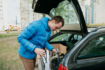 Side view of man holding umbrella while standing by car