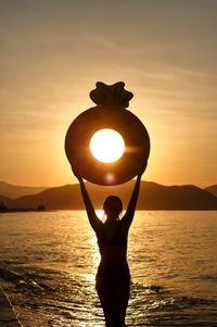 Silhouette woman standing by sea against sky during sunset