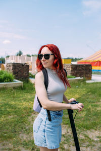 Young bright woman smiles and rides electric scooter in the summer in the city