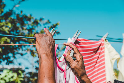 Cropped hands of woman hanging laundry on clothesline against clear blue sky