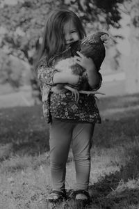 Full length portrait of girl holding chicken bird on field