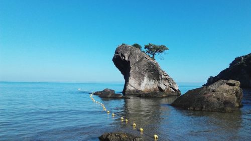 Rock formation in sea against clear blue sky