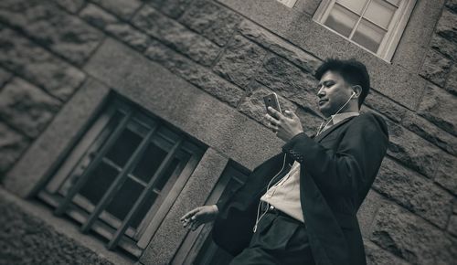 Low angle view of businessman listening to music through smart phone against building