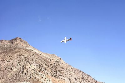 Low angle view of airplane over rocky mountains against sky