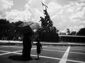 Rear view of woman with son under umbrella walking at war memorial 