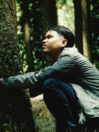 Side view of young man looking away while crouching in forest