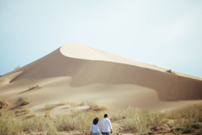 Rear view of man on sand dune against clear sky