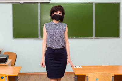 A teacher at the blackboard in a school classroom in a protective black mask during the pandemic.