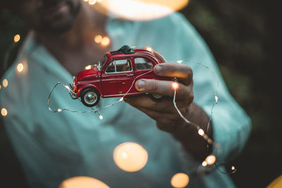 Midsection of man holding illuminated string light and toy car