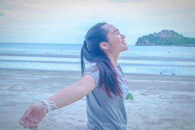 Side view of young woman standing at beach against sky