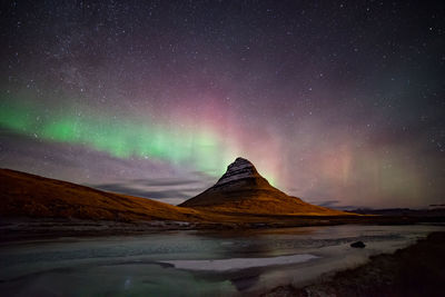 Scenic view of sea by mountain against sky at night