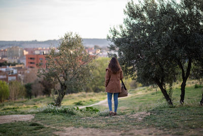 Rear view of woman standing on land by trees against sky