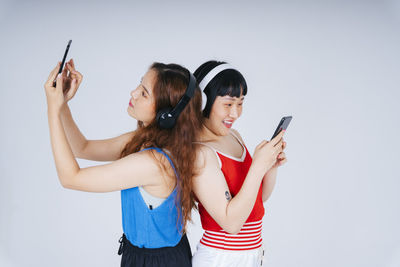 Lesbian couple using phone while listening music against gray background