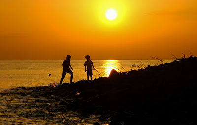 Silhouette people on beach against sky during sunset