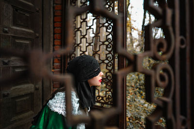 Portrait of young woman in halloween costume looking through window in autumn forest