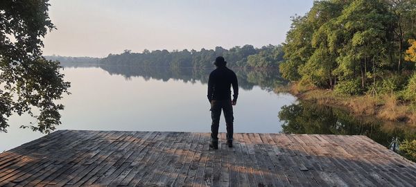 Rear view of man standing by lake against sky