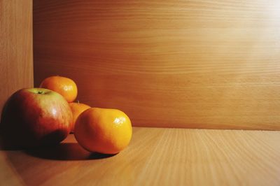 Close-up of apple and oranges on wooden table against wall