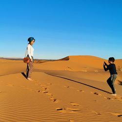 Man standing on sand dune in desert against clear sky