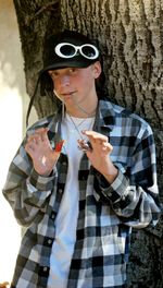 Portrait of teenage boy holding chains while standing against tree trunk