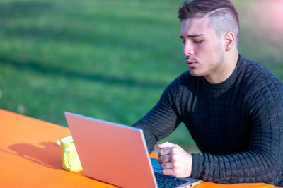 Young man using laptop while sitting on field