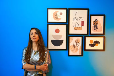 Portrait of young woman standing against blue background