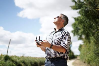 Side view of man holding remote control against sky