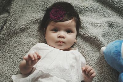 High angle portrait of cute baby girl lying down on carpet at home