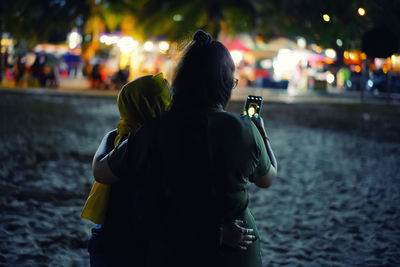 Rear view of couple kissing on street at night