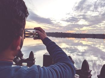 Portrait of man photographing through mobile phone against sky