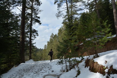 Man walking on snow covered land against sky