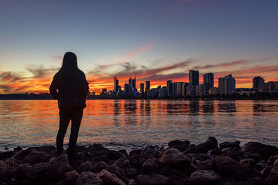 Silhouette man standing on rock by sea against sky during sunset