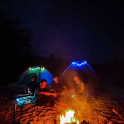 People sitting by bonfire against sky at night