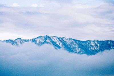 Scenic view of snow covered mountains amidst fog against cloudy sky