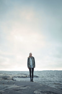 Full length portrait of wonderlust woman standing on rock by sea