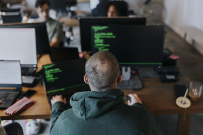 Rear view of male programmer coding on computer at creative office