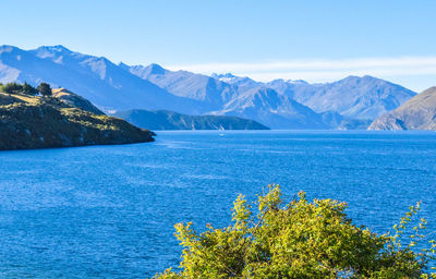 Scenic view of sea and mountains against clear blue sky