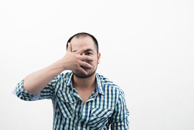 Portrait of mid adult man covering face against white background