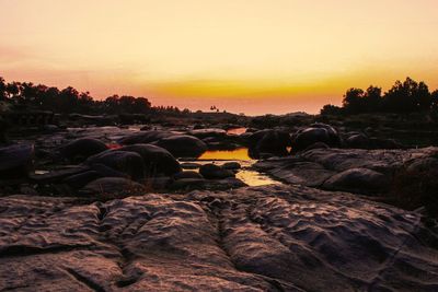 Rocks at beach against sky during sunset