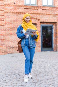 Full length portrait of woman standing against brick wall