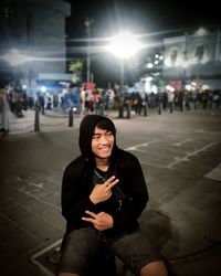 Portrait of young woman sitting on street at night