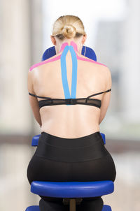 Rear view of mature woman with pink kinesio tape sitting on neck massage chair