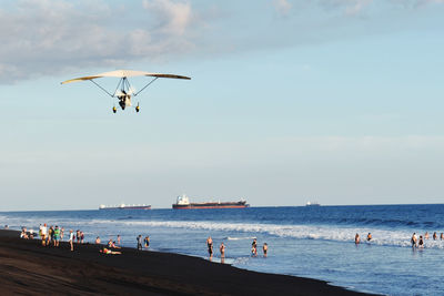 People enjoying at beach against sky, a plane and boats