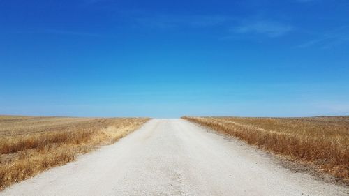 Road amidst field against clear blue sky