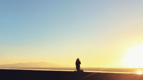 Silhouette person standing on landscape against clear sky during sunset