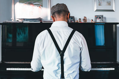Rear view of man sitting by piano at home