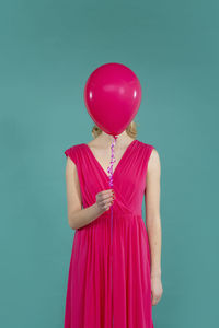 Young woman holding balloon in front of face standing against green background