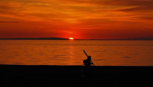 Silhouette man on sea against orange sky during sunset