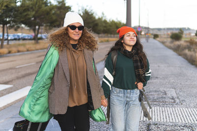 Happy mother and daughter holding hands walking on road